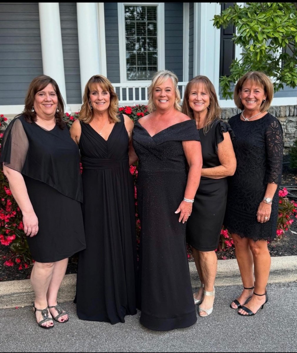 Five women in black formal dresses standing together outdoors.